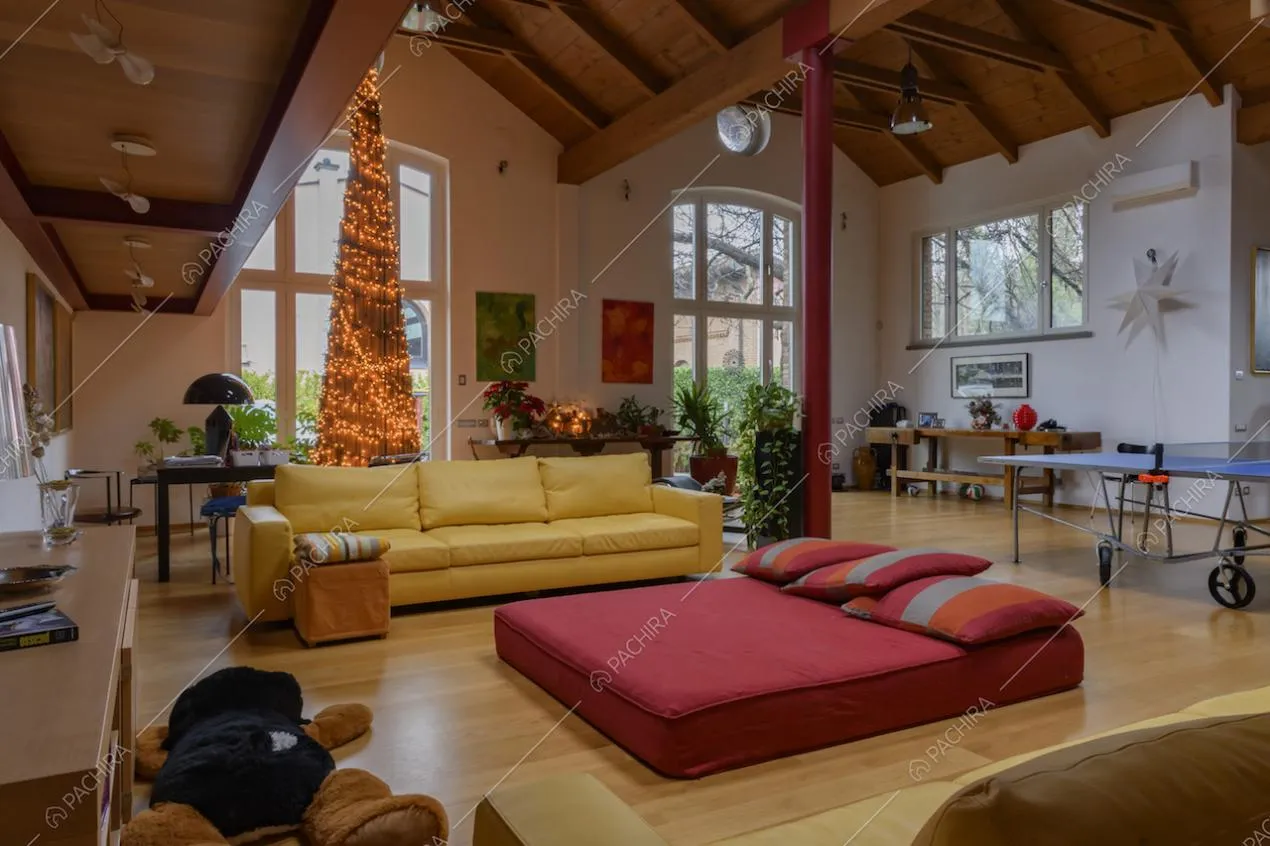Luminosa sala con divani gialli, pouf rosso e soffitto con lucernari e travi in legno a vista