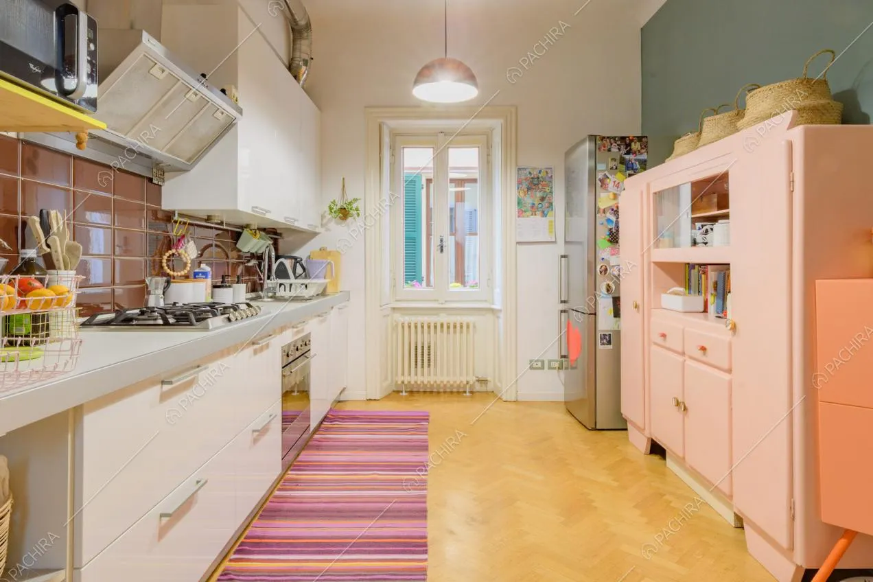 Parete azzurra, credenza rosa e fornelli a gas nella cucina con pavimento in parquet a spina di pesce