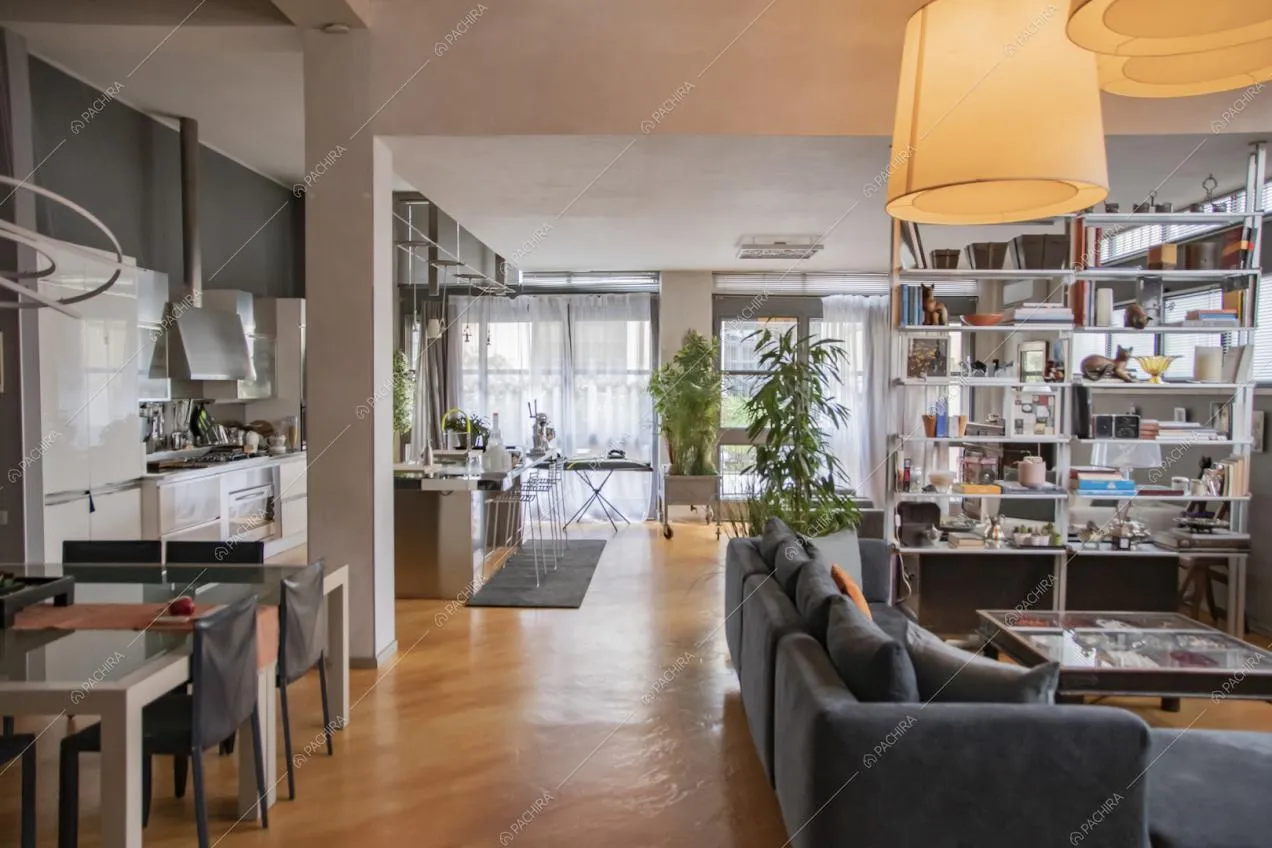 Divano angolare, tavolo da pranzo e isola della cucina nell'open space dalle pareti bianche