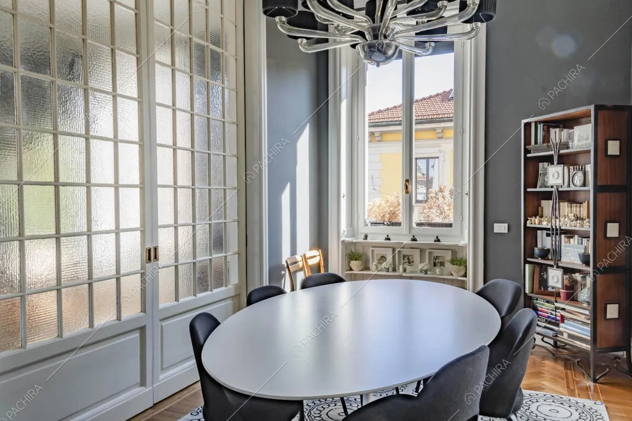 Luminosa sala da pranzo con tavolo bianco, pavimento in parquet a spina di pesce e porte a vetri