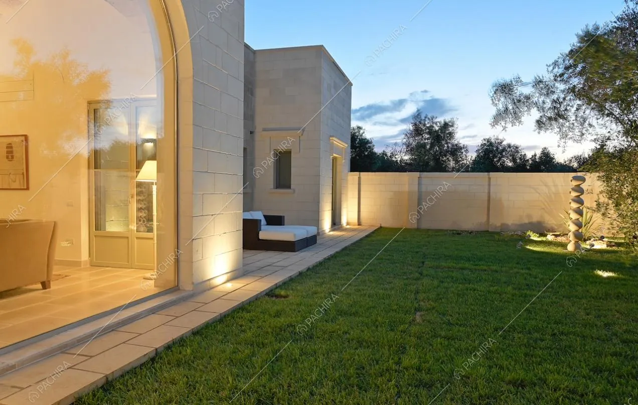 Curatissimo giardino con illuminazione da esterno, circondato dalle mura bianche della casa e vista sul salotto tramite ampia vetrata