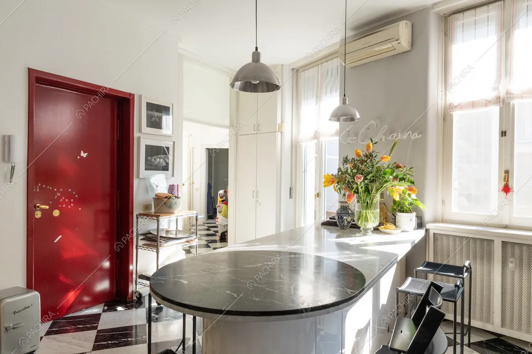 Porta d'ingresso rossa nella cucina con pavimento a scacchi, penisola con piano in marmo e sgabelli