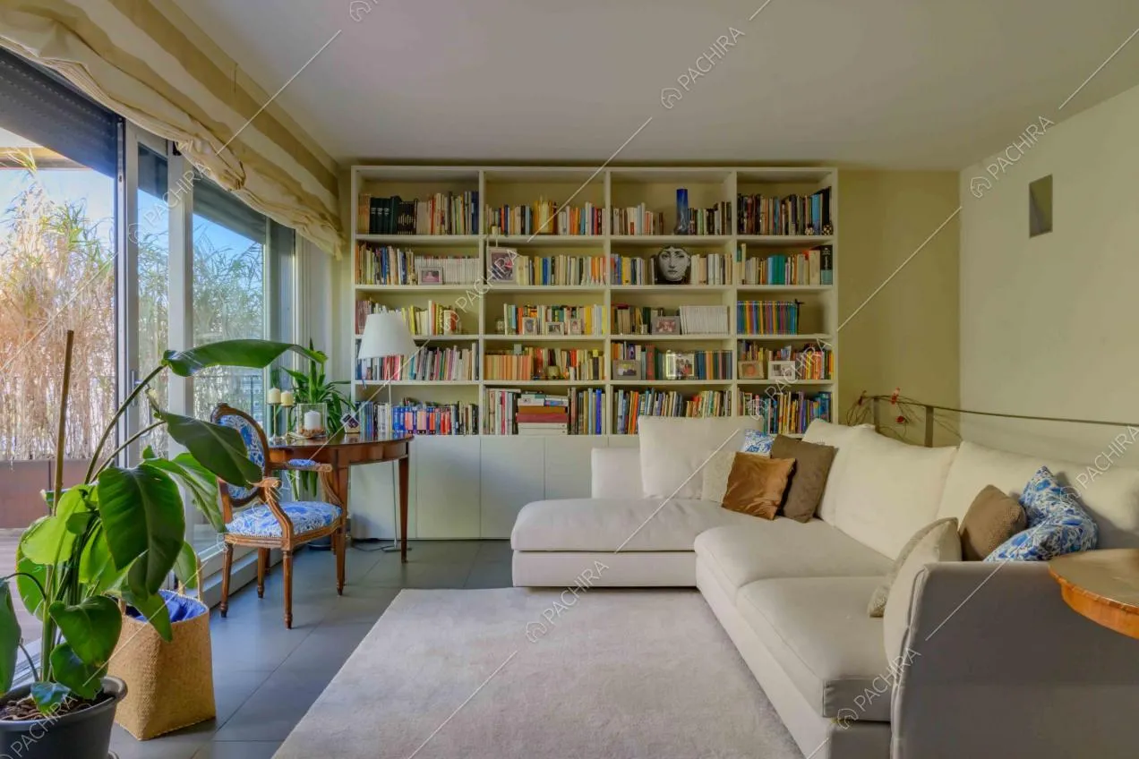Soggiorno con divano bianco angolare, libreria e porta-finestra scorrevole che conduce alla terrazza