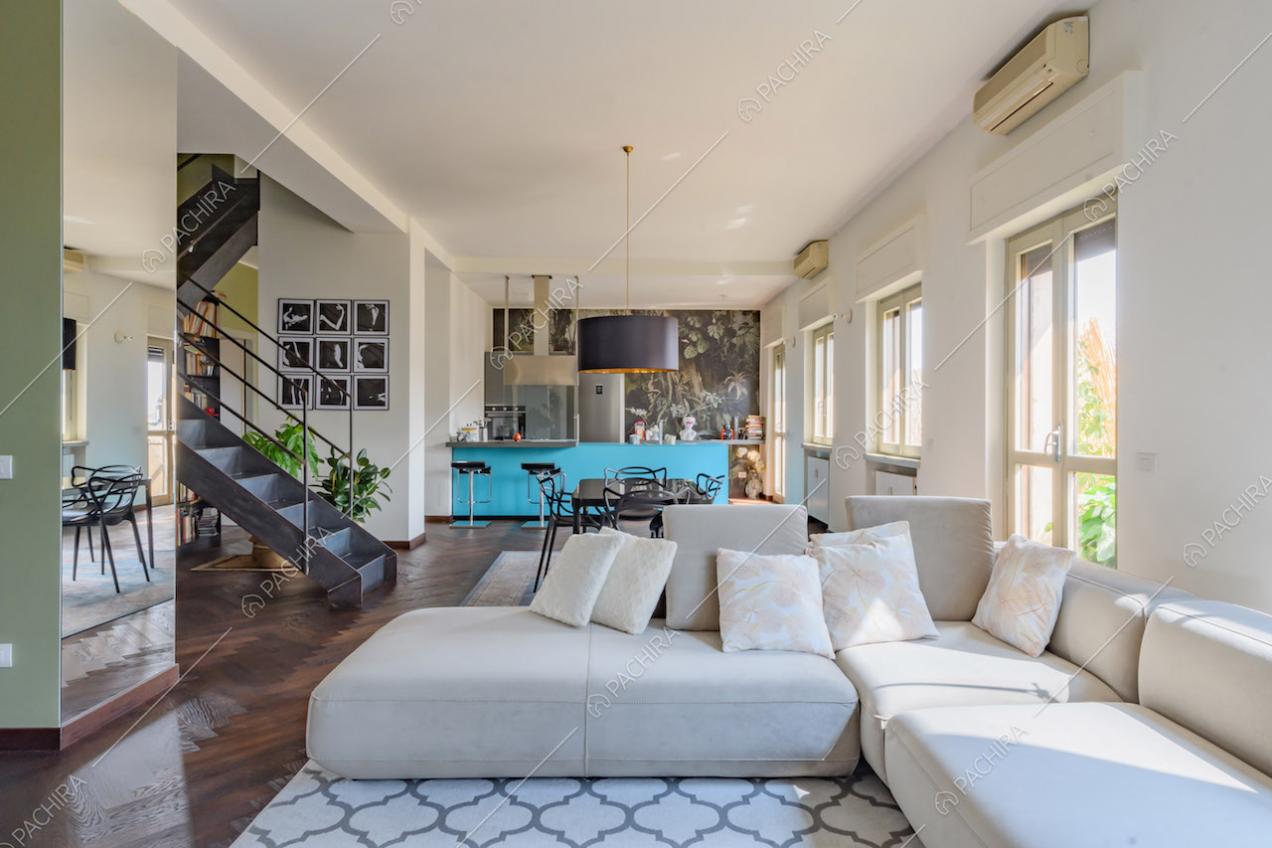 Divano angolare bianco nella sala con pavimento in parquet e colonna con specchio