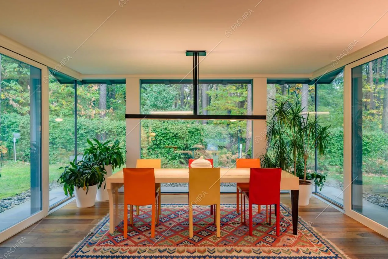 Tavolo da pranzo bianco con sedie colorate circondato da vetrate con vista sul giardino