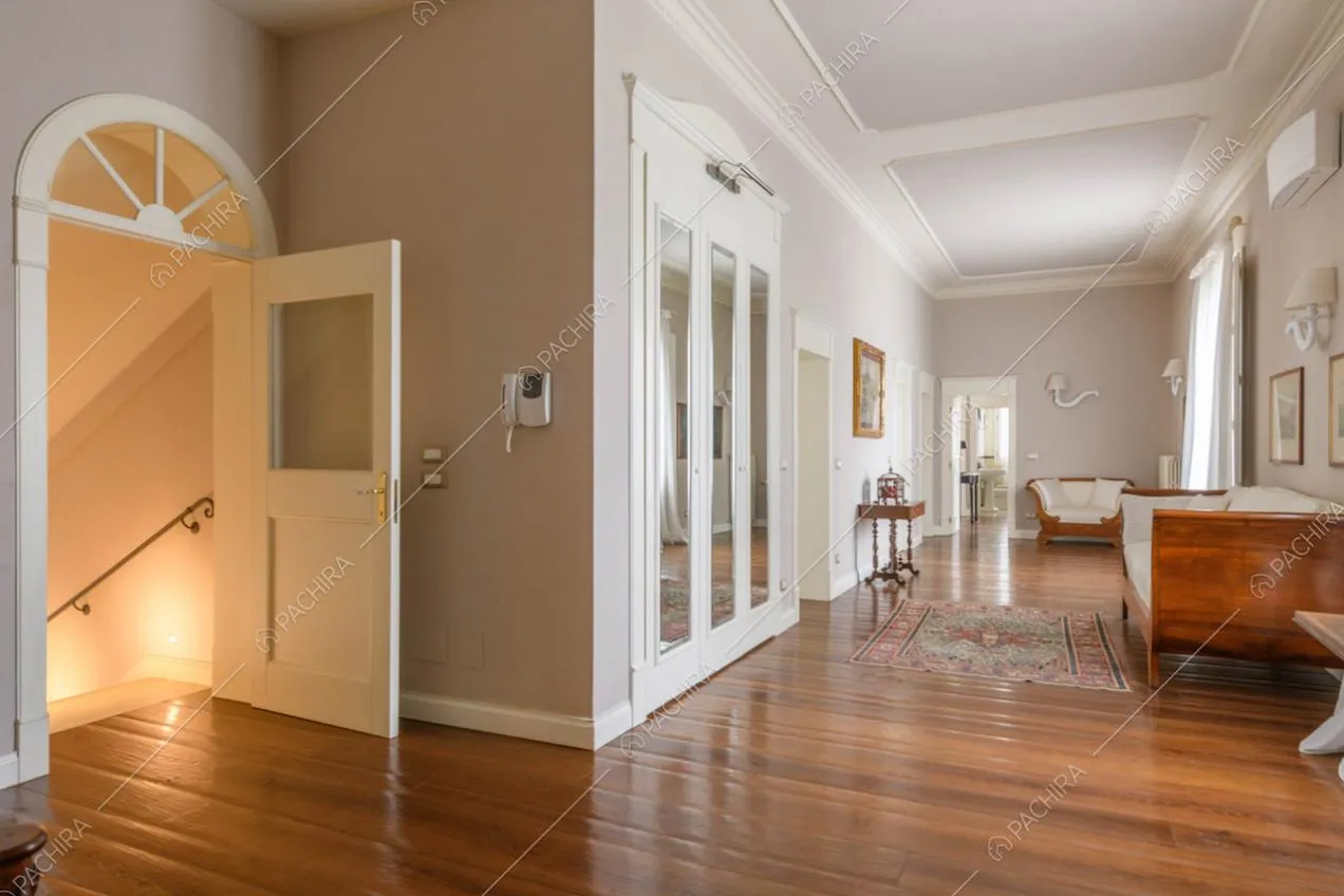 Pavimento in parquet nel luminoso corridoio con divani, porta a vetri e vista sulle scale