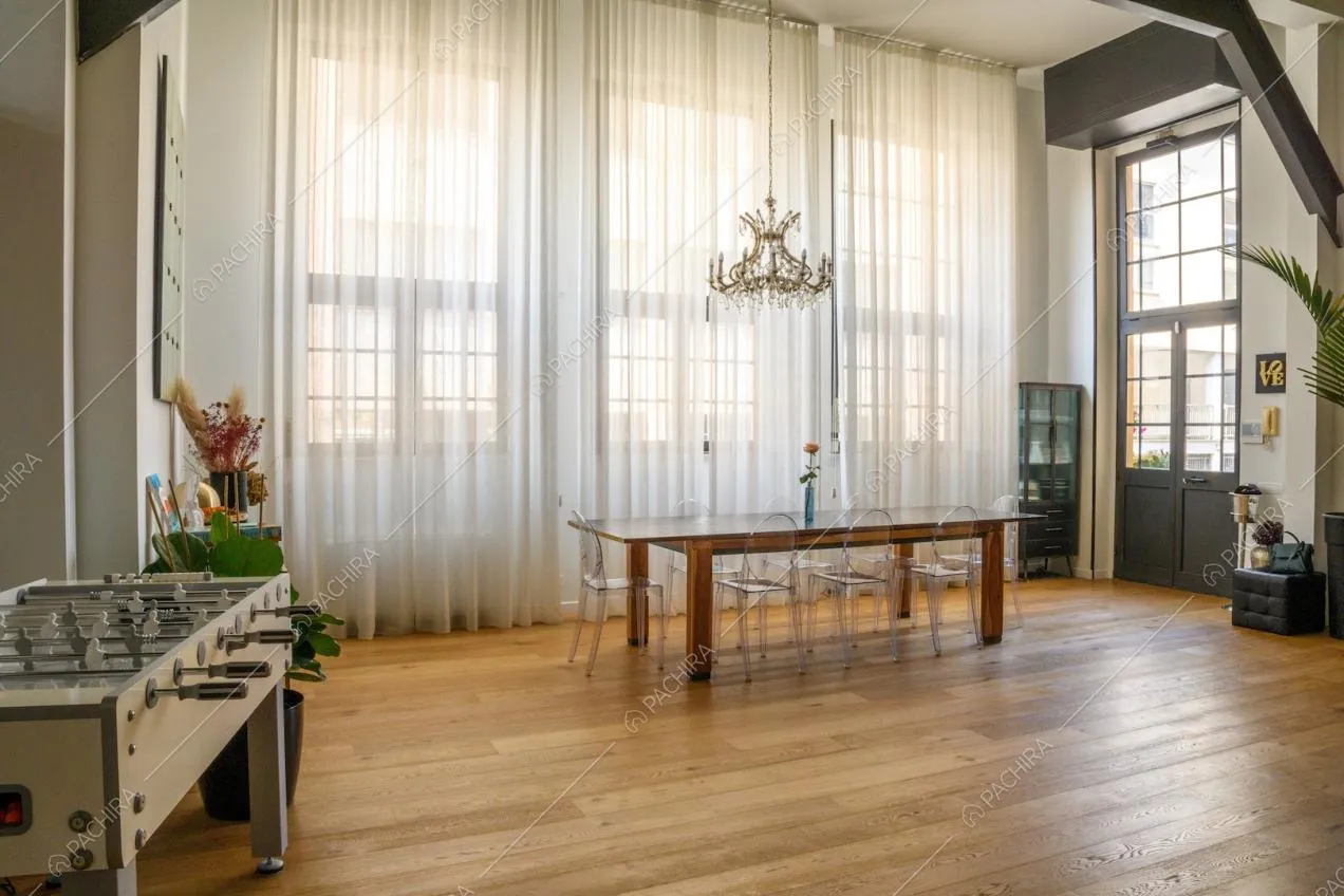 Soggiorno illuminato dalle ampie vetrate in stile industriale con pavimento in parquet e tavolo da pranzo in legno
