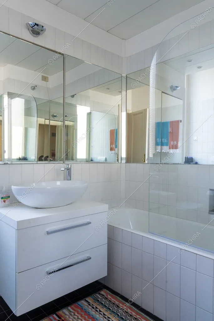 Bagno con soffitto in travi in legno bianco a vista, vasca con piastrelle e specchi