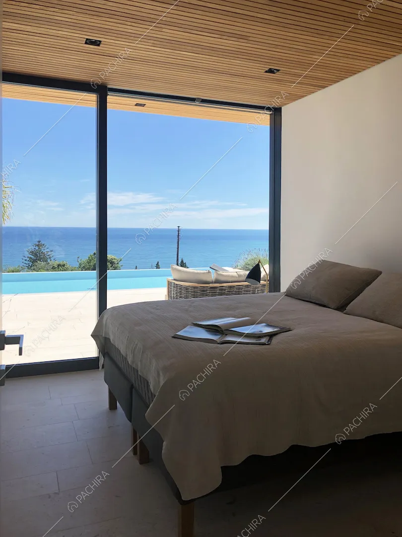 Camera da letto matrimoniale in stile minimal con parete bianca, soffitto in legno e vista sulla piscina e sul mare