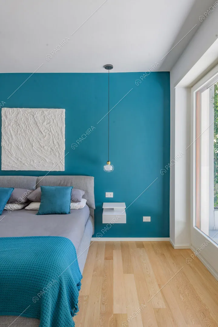 Letto matrimoniale nella luminosa camera con parete azzurra e vetrate