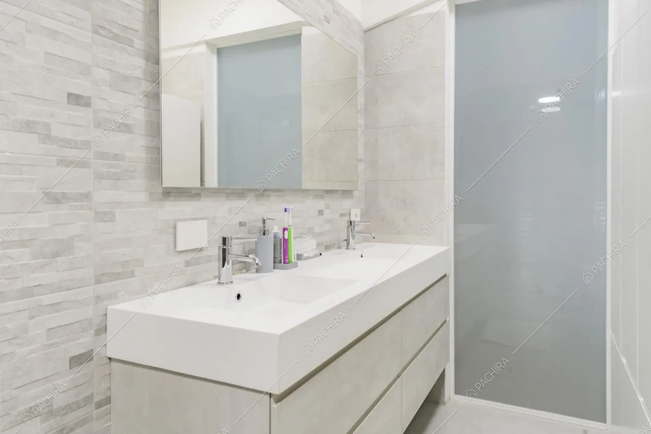 Nel bagno dai toni neutri e dal pavimento in pietra troviamo un doppio lavandino e un ampio specchio