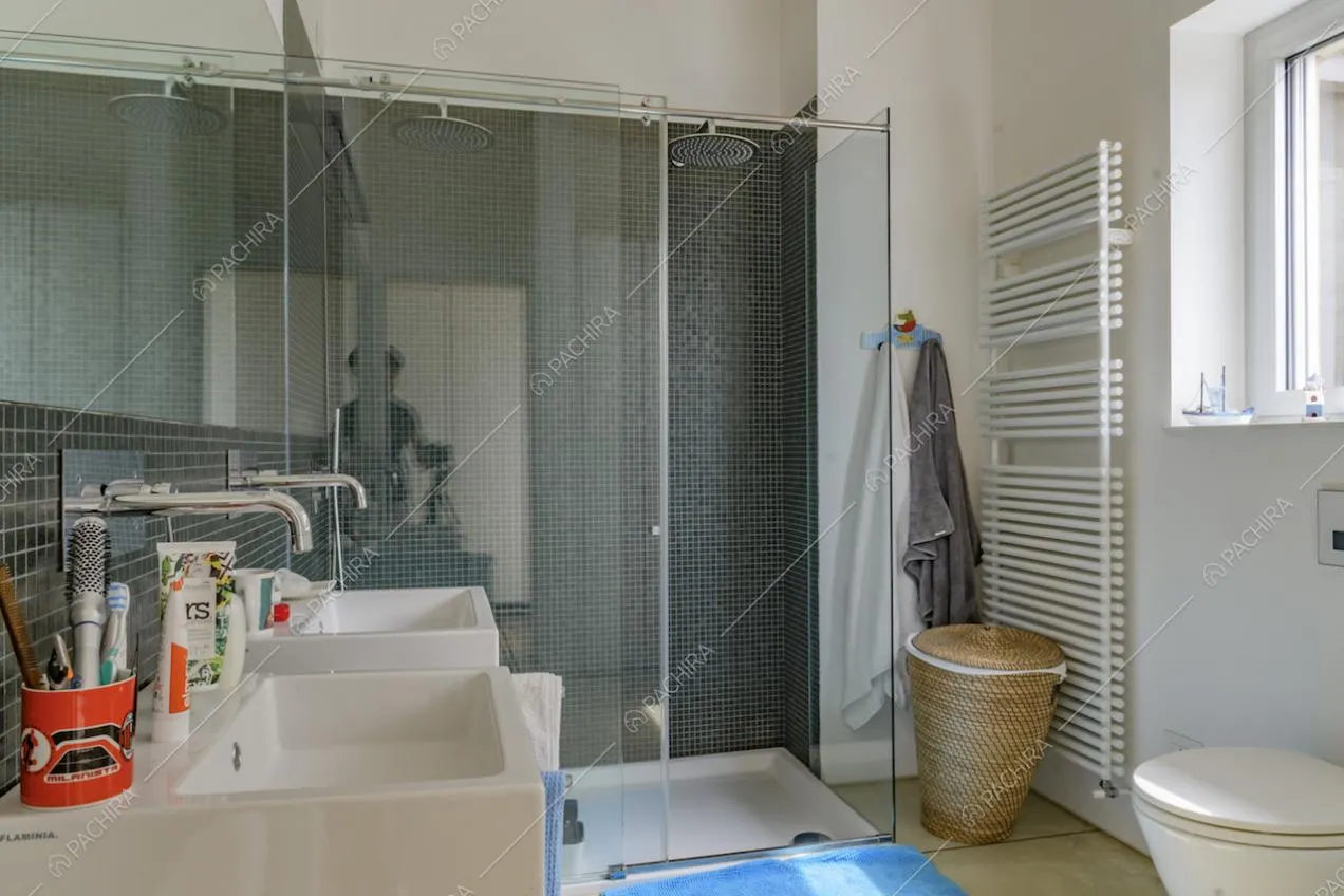 Nel bagno dalle pareti bianche, ampio box doccia con piastrelline blu e doppio lavandino