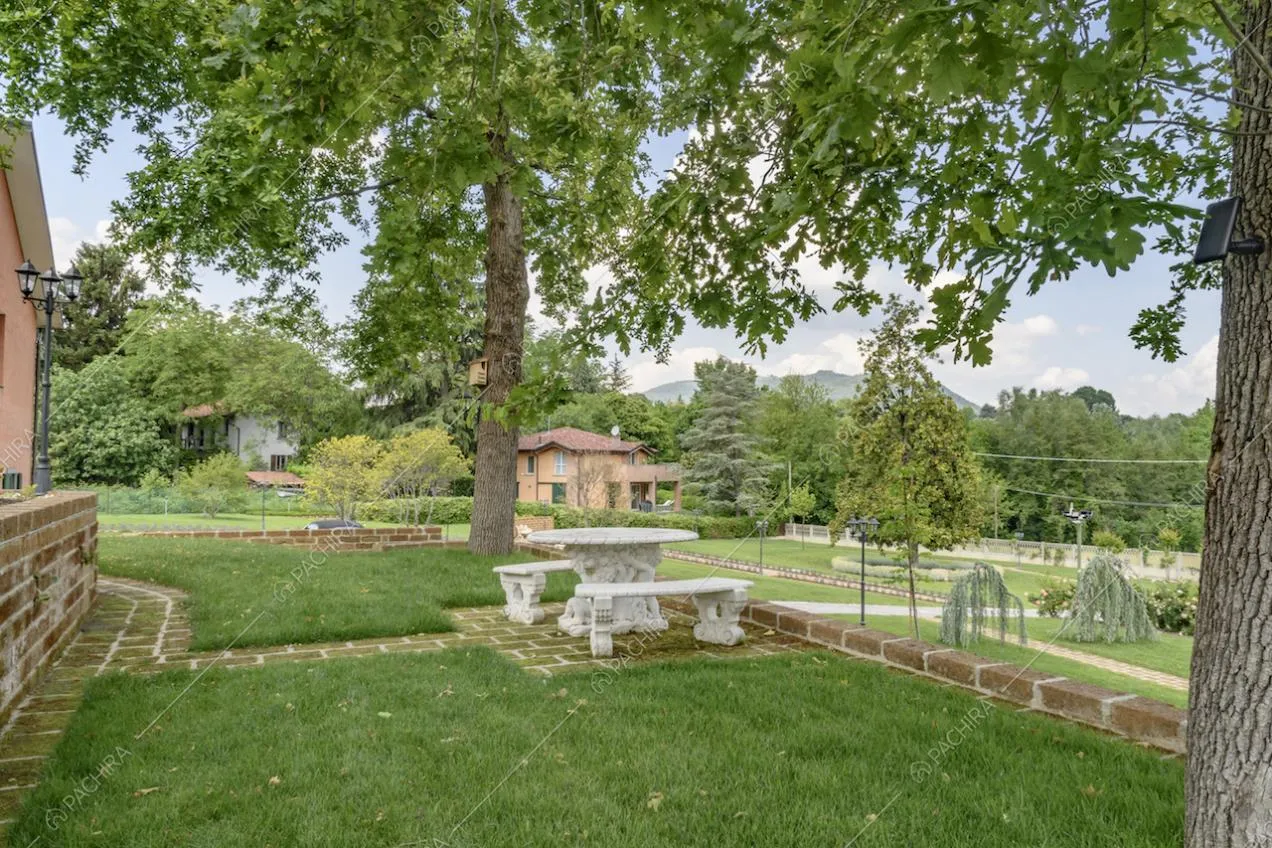 Ampio parco della villa con prato curato, vialetto in mattoni, e panchine e tavolo da esterno bianchi
