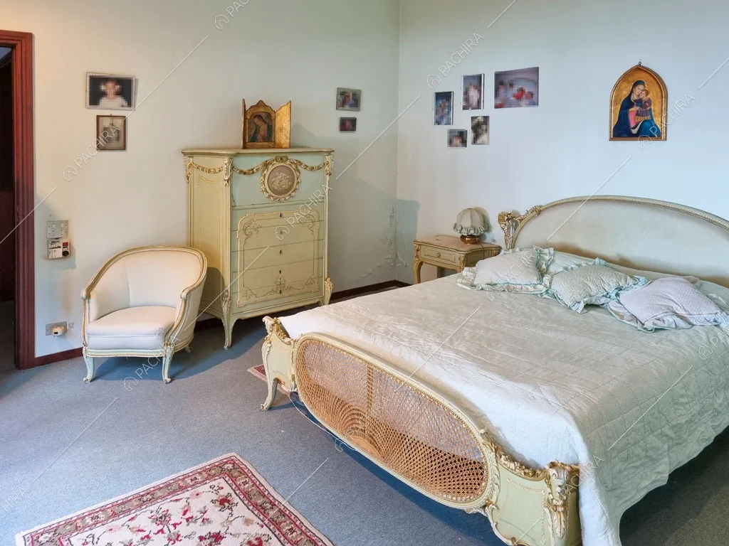 Letto matrimoniale nella camera con pareti bianche e pavimento in moquette grigia