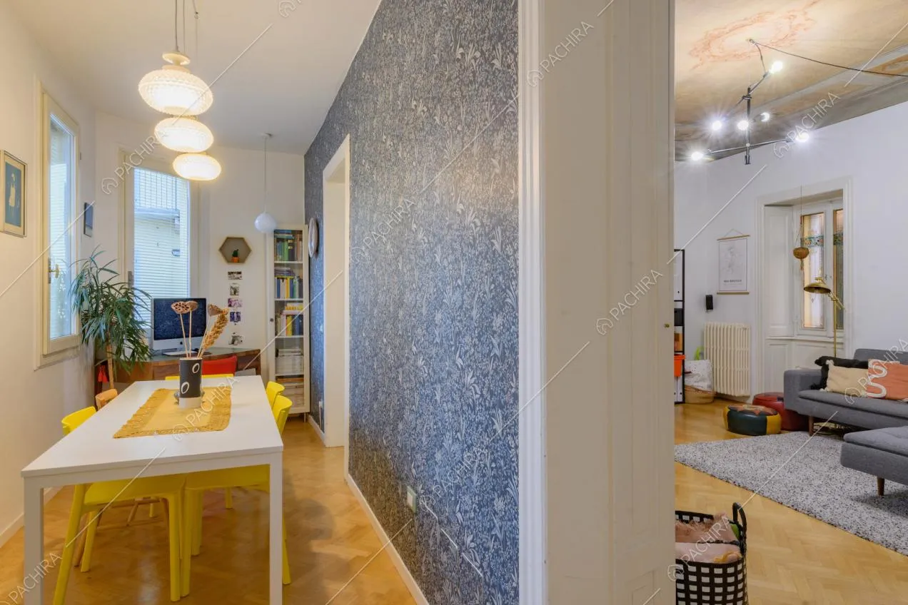 Sala da pranzo con carta da parati blu, tavolo bianco e vista sulla zona living