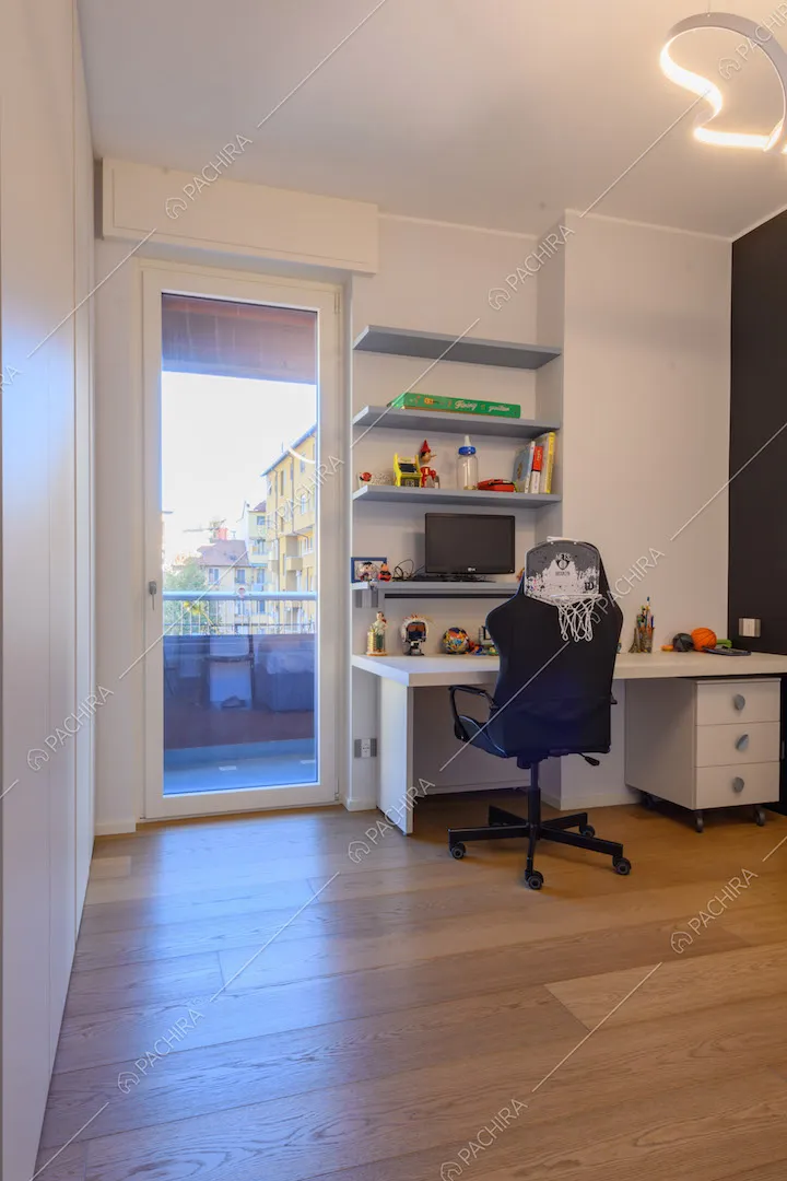 Scrivania bianca nella camera con pavimento in parquet e porta-finestra per accedere al balcone