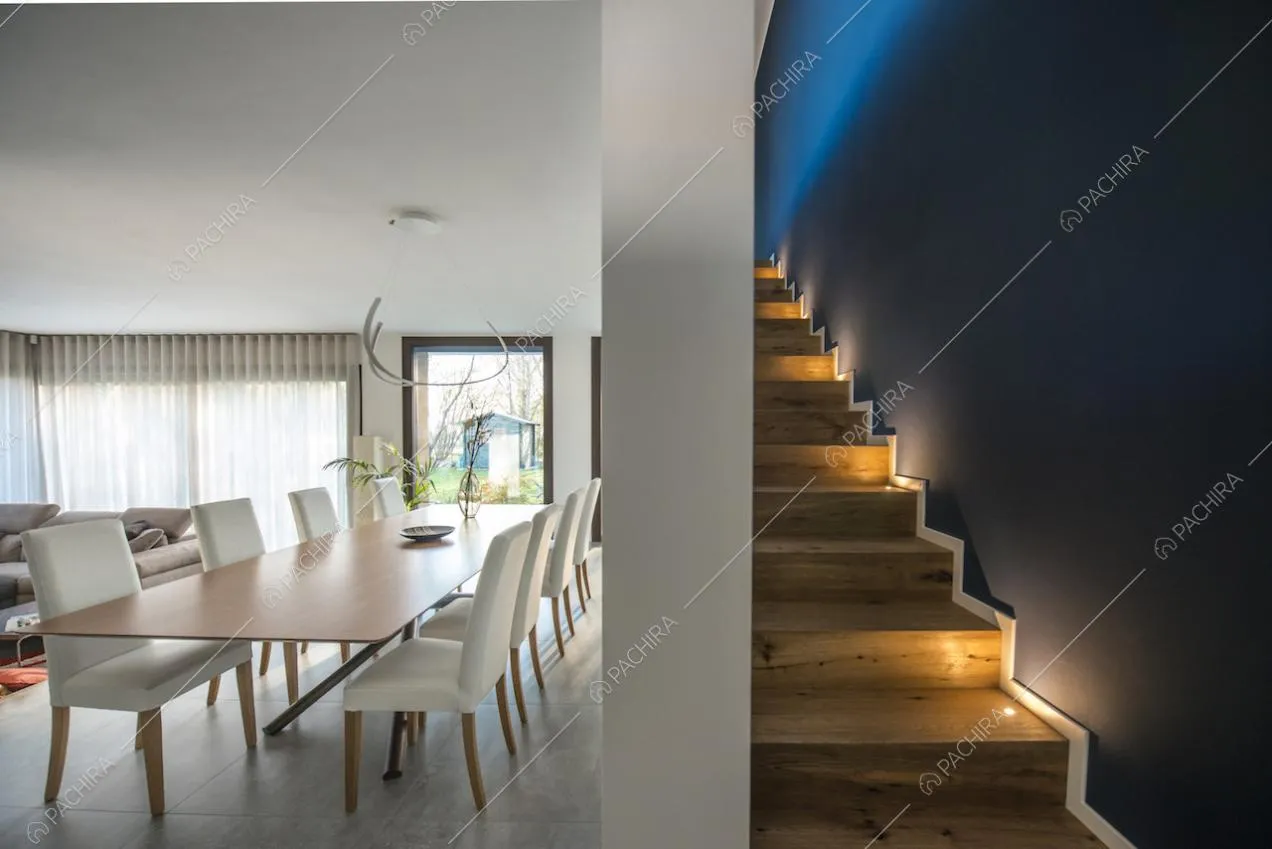 Vista su sala da pranzo con vetrate e su scale con luci segnapassi laterali e parete blu