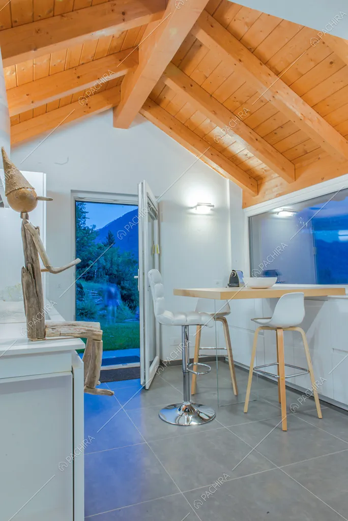 Cucina dalle pareti bianche con soffitto dalle travi in legno a vista, bancone in legno e sgabelli