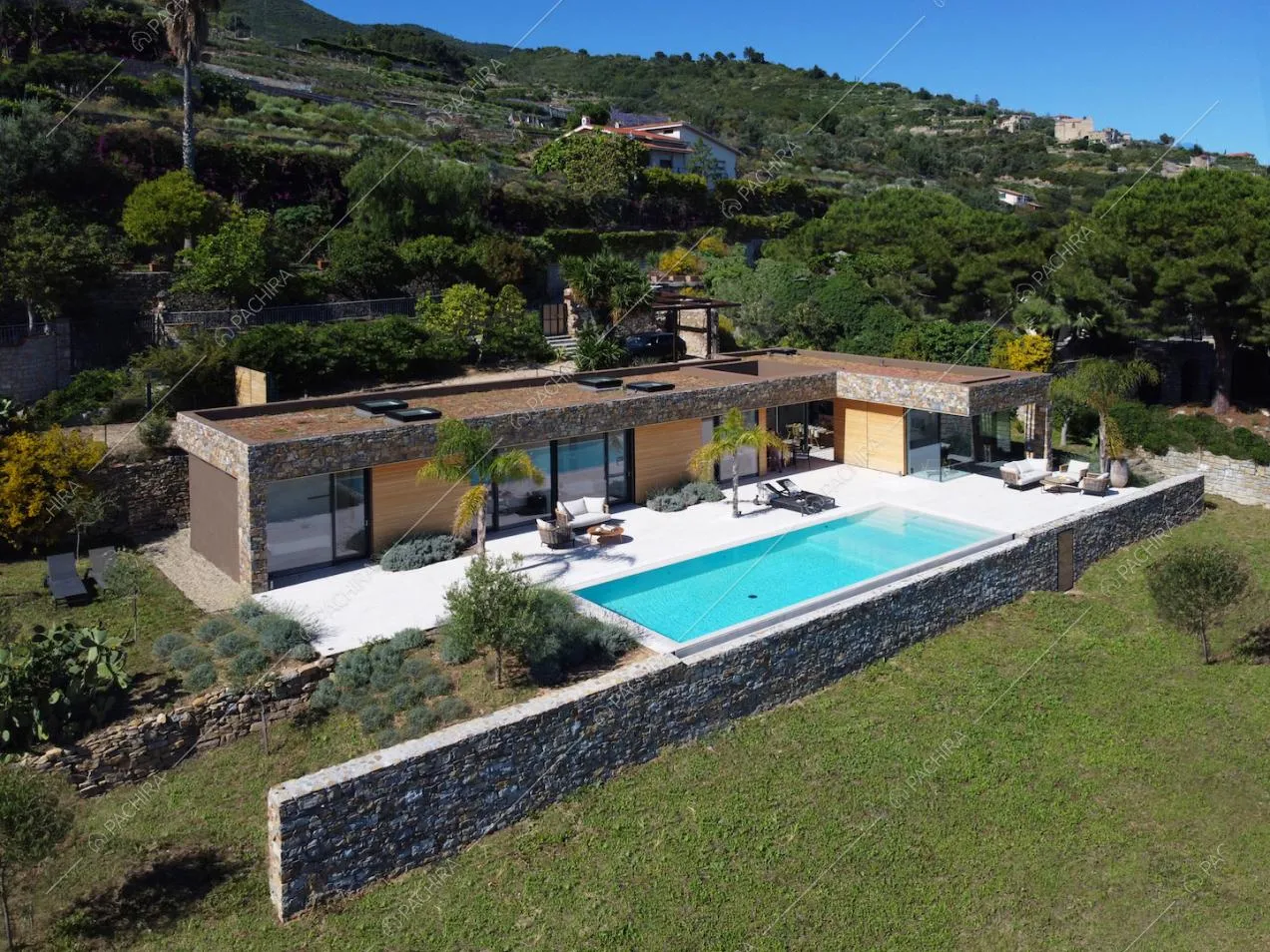 Vista dall'alto sugli esterni della location con muro di pietra, sulla piscina e sul tetto piatto con lucernari