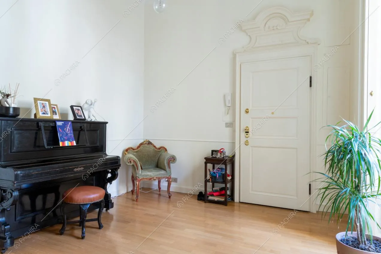 Atrio con pavimento in parquet, pianoforte nero a muro e porta d'ingresso bianca con boiserie