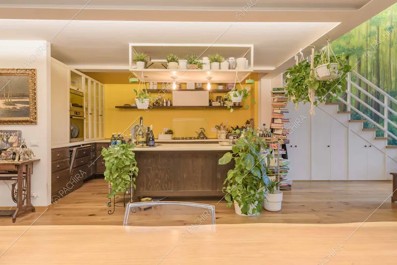 Dal tavolo da pranzo vista sulla cucina con isola, parete gialla e fornelli a gas