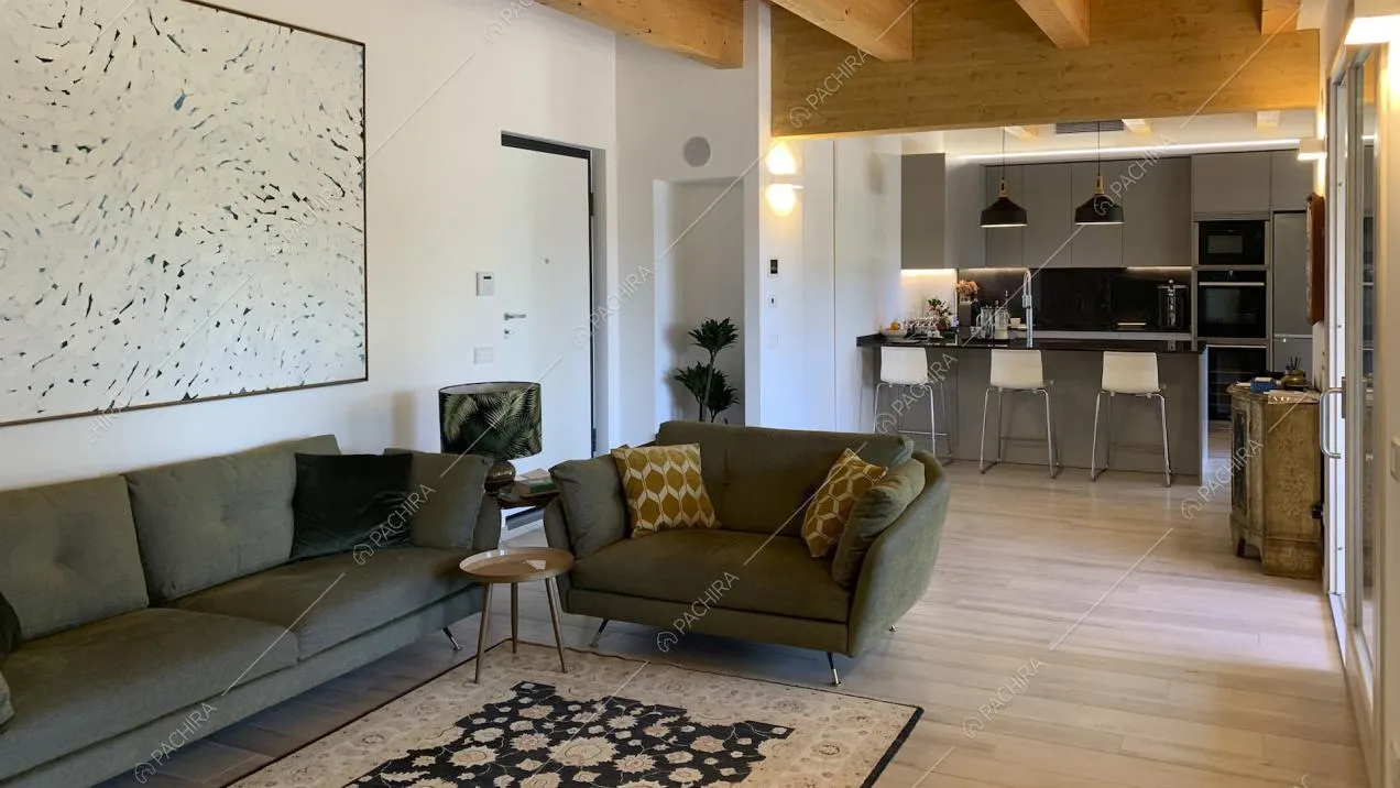 Zona giorno open space con divano, poltrona, grande quadro astratto e cucina a vista