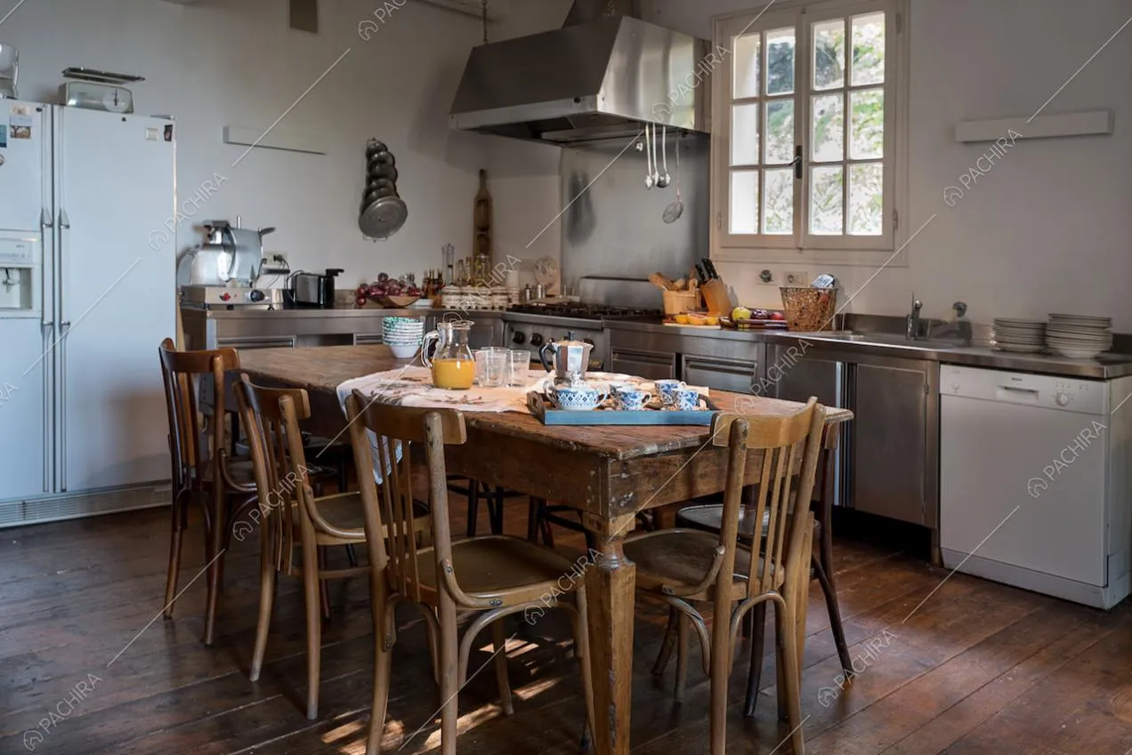 Tavolo da pranzo in legno nella cucina industriale con fornelli a gas e pareti bianche