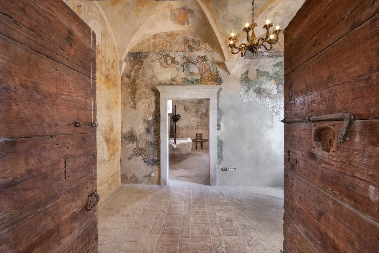 Accesso tramite portone in legno a sala affrescata con pavimento in cotto e vista sulla cucina