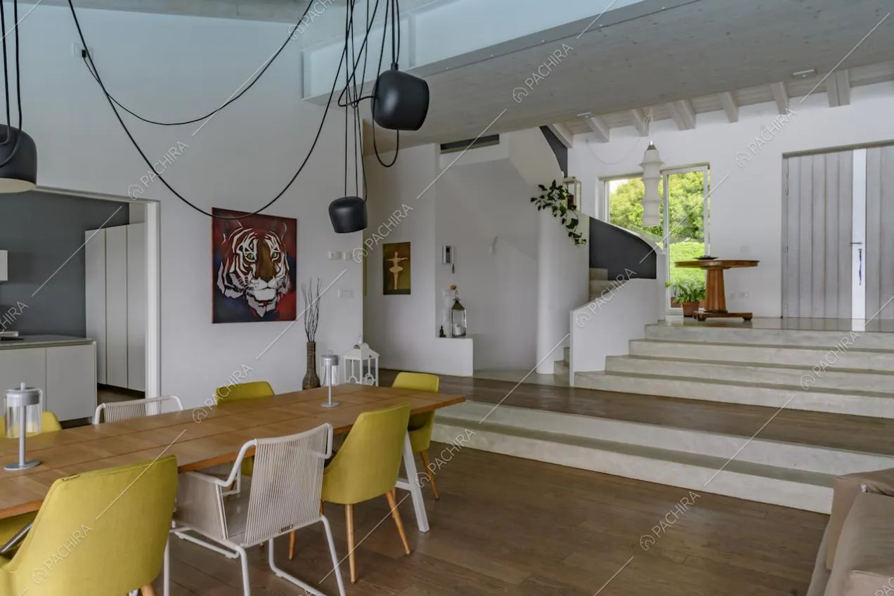Tavolo da pranzo in legno con sedie bianche e gialle, nella sala dalle pareti bianche con vista su cucina e scale