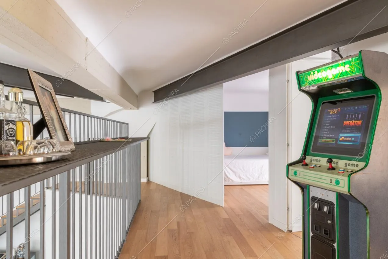 Videogioco acade sul soppalco con pavimento in parquet, balaustra in metallo e vista su camera da letto