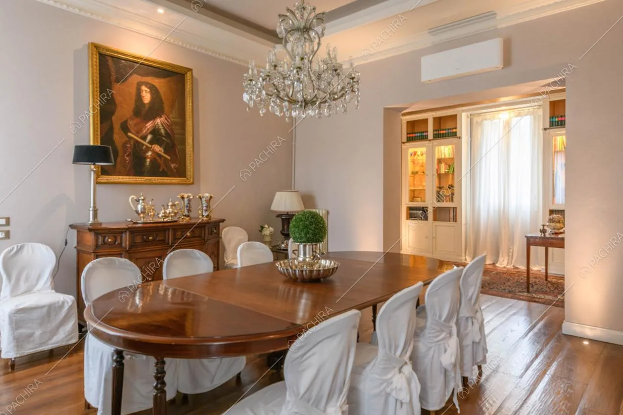 Sala da pranzo con tavolo in legno, sedie bianche e lampadario antico in cristallo