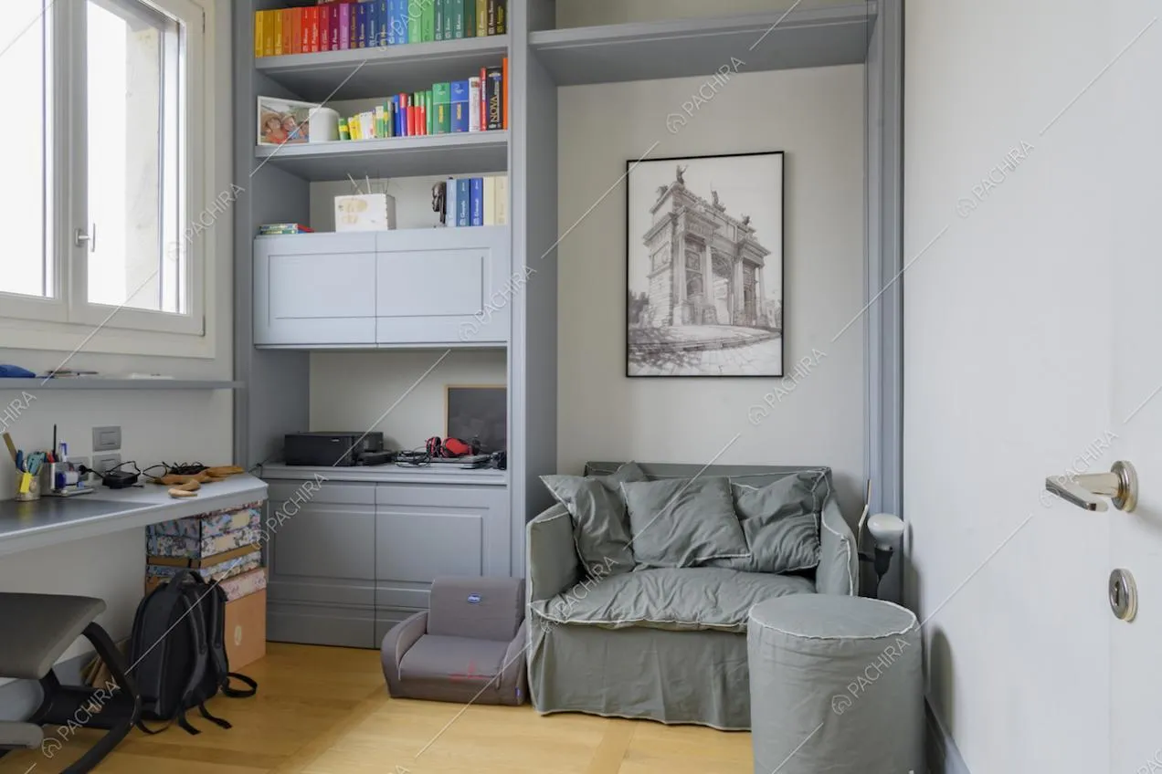 Camera da letto con pavimento in parquet, libreria grigia con boiserie, divano e pouf