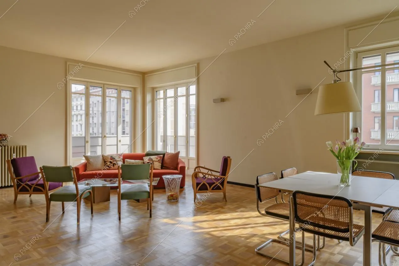 Pavimento in parquet nel soggiorno con poltrone colorate, divano rosso e tavolo da pranzo bianco