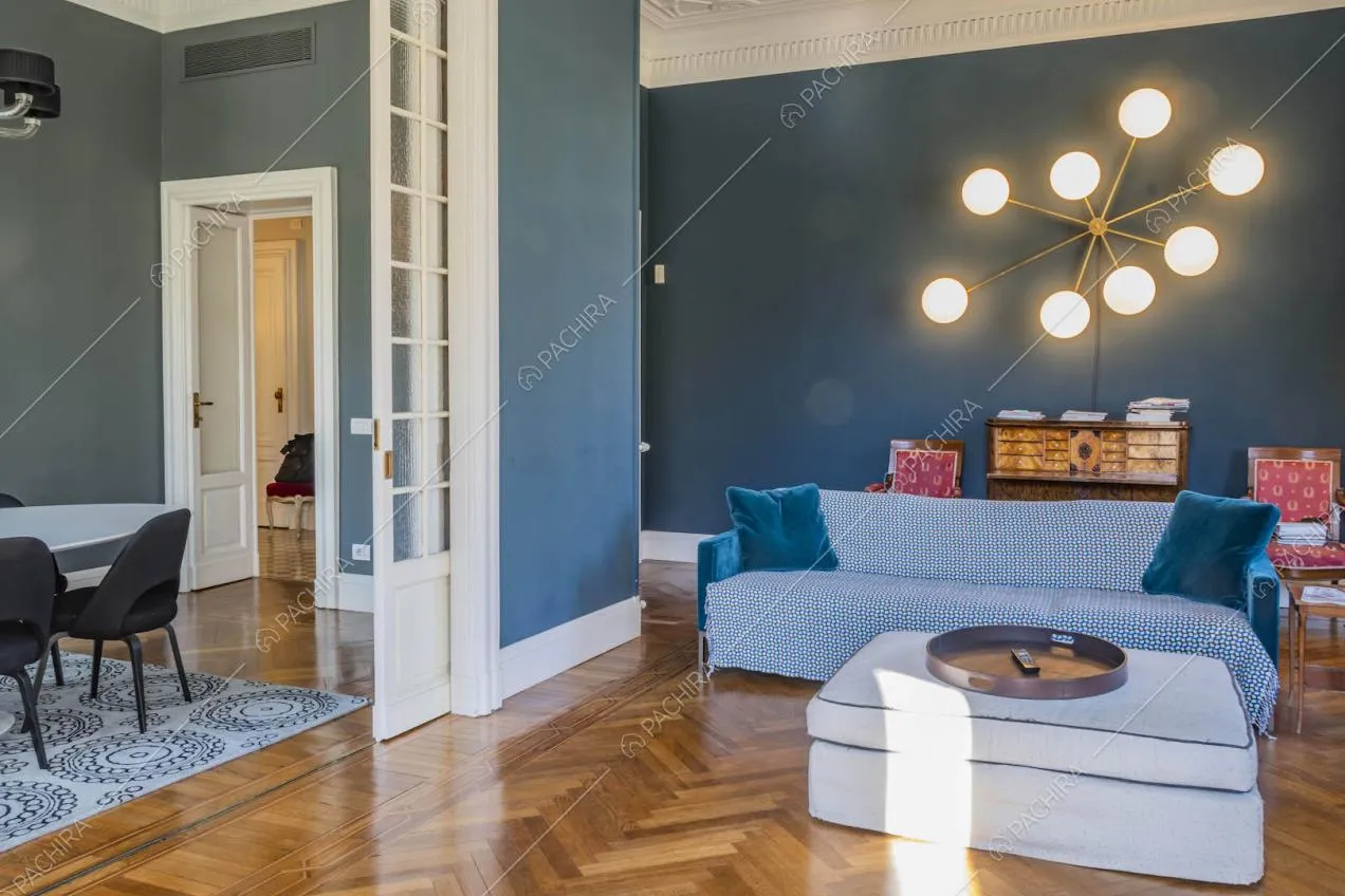 Pouf bianco e divano blu nel salotto con pavimento in parquet e vista sulla sala da pranzo