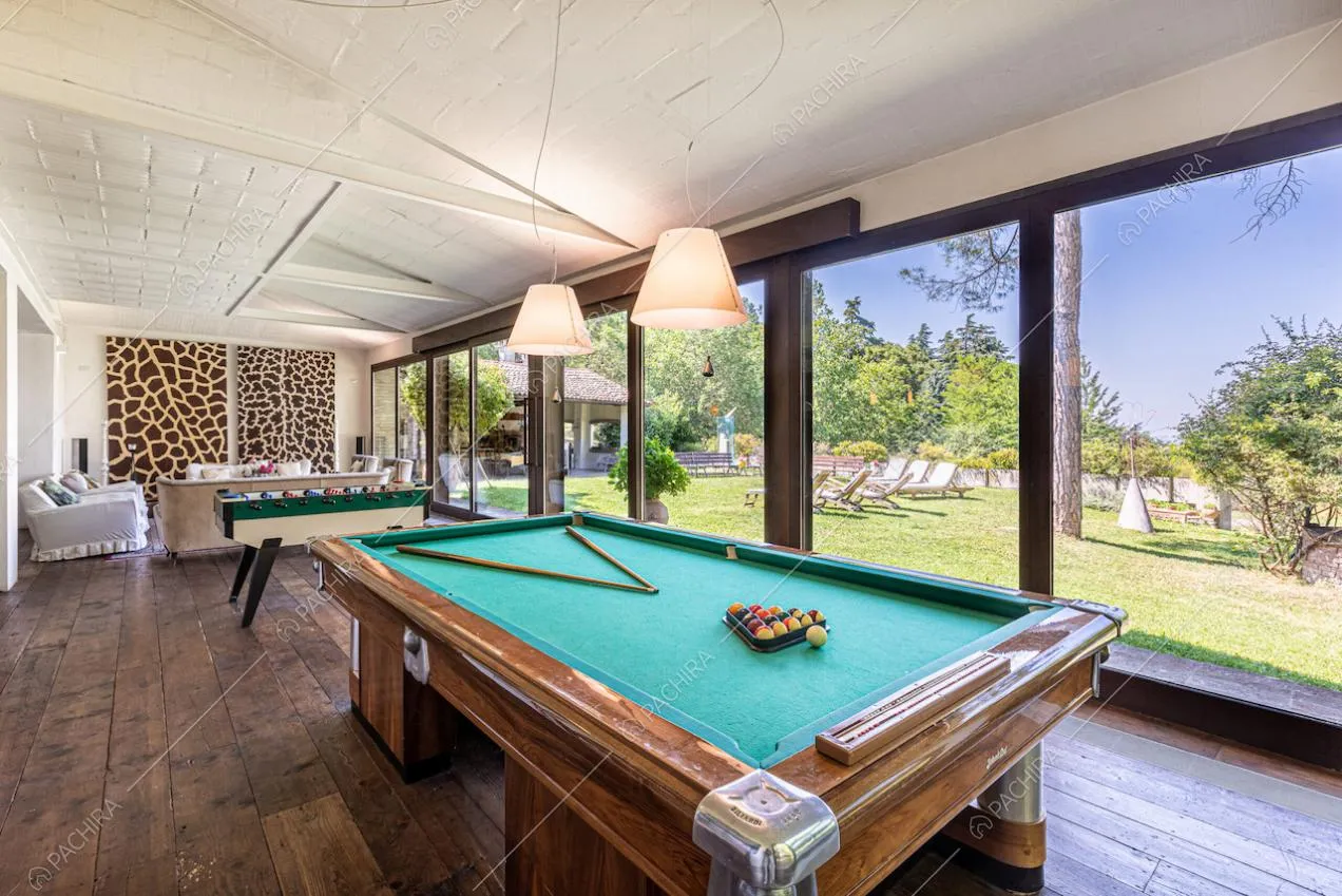 Sala con biliardo e divani, dal pavimento in parquet, soffitto bianco e porte-finestre scorrevoli