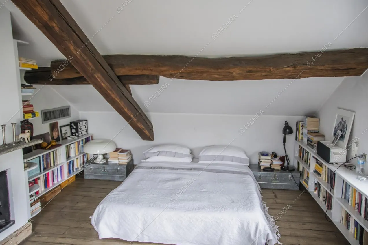 Letto matrimoniale sotto alle travi a vista e mobiletti bassi con libri