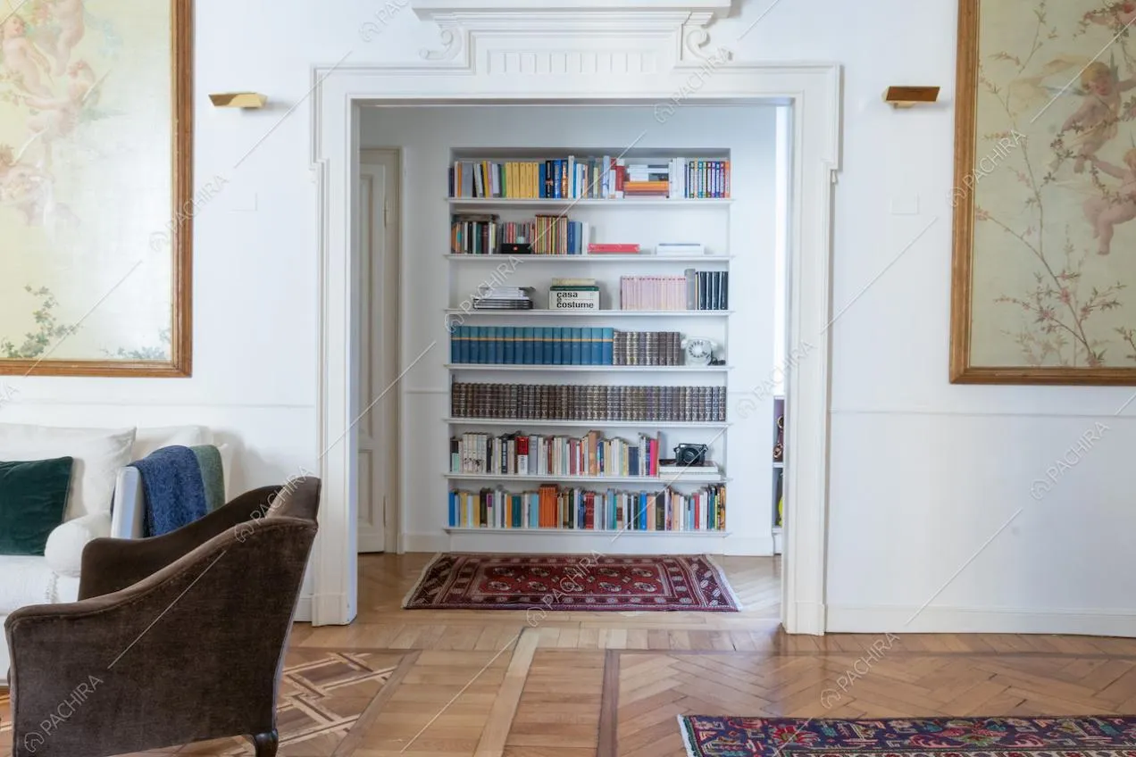 Dal salotto con poltrone marroni vista sulla libreria e sul pavimento in parquet