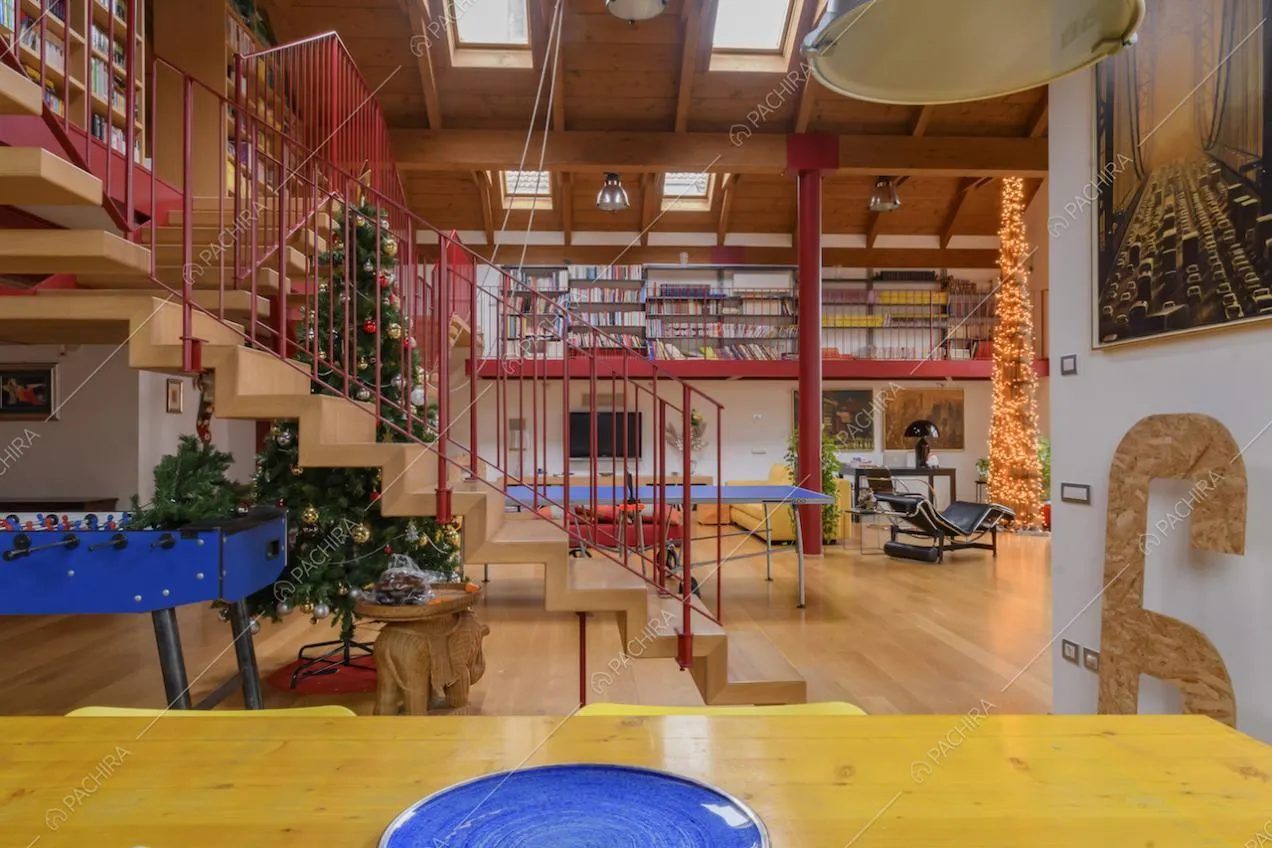 Dal tavolo giallo da pranzo vista sul grande salone con scale, pavimento in parquet e lucernari