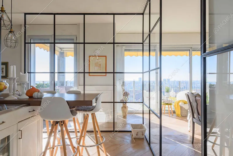 Cucina con parete vetrata in stile industriale e vista sul salotto con vetrate