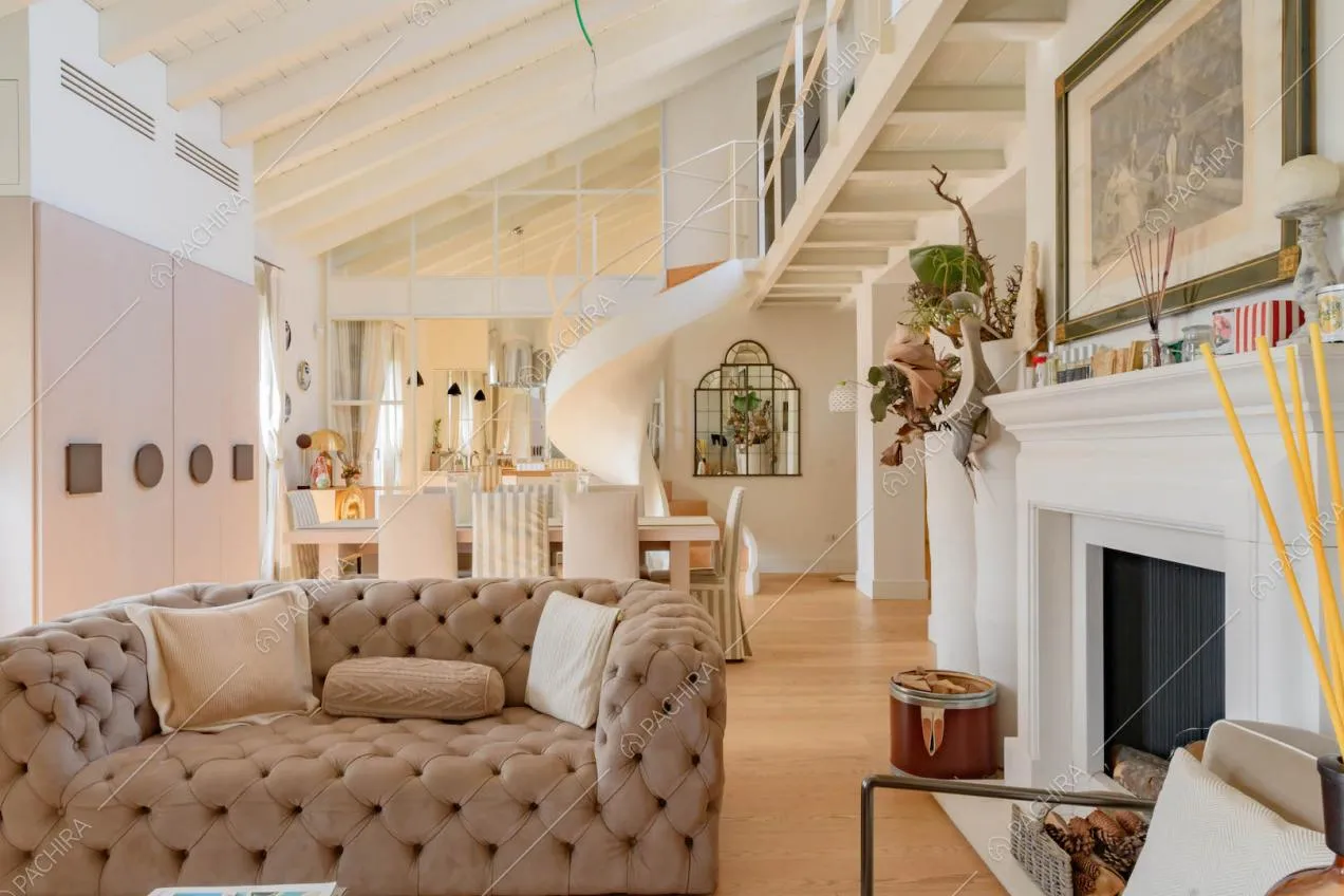 Divanetto beige nella zona living con travi bianche a vista sul soffitto e scala a chiocciola
