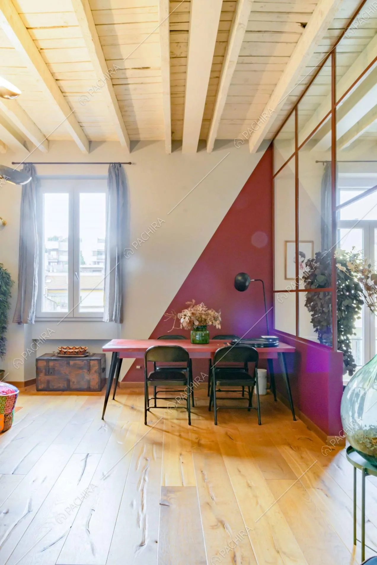 Nell'ampio salone dal pavimento in parquet tavolo da pranzo rosso, sedie nere e vetrate in stile industriale