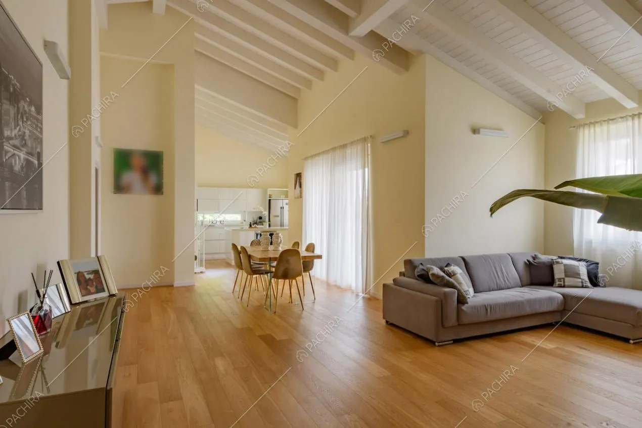 Luminosa zona living con divano grigio angolare, pareti gialle e travi a vista