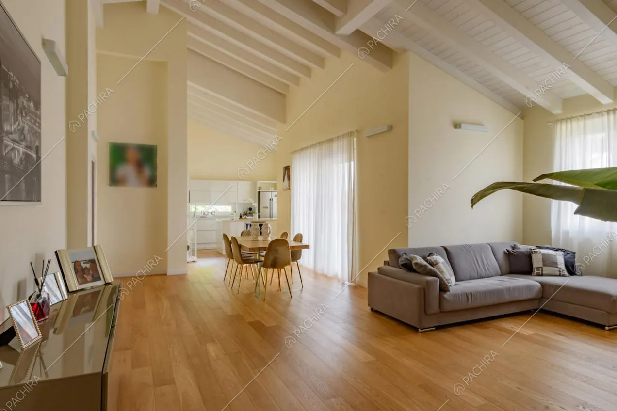 Luminosa zona living con divano grigio angolare, pareti gialle e travi a vista