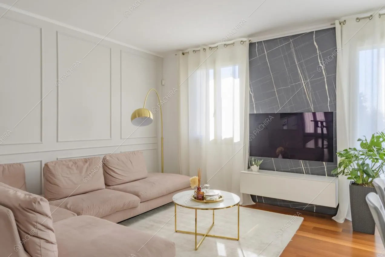 Salotto con boiserie alle pareti, divano angolare rosa e pavimento in parquet
