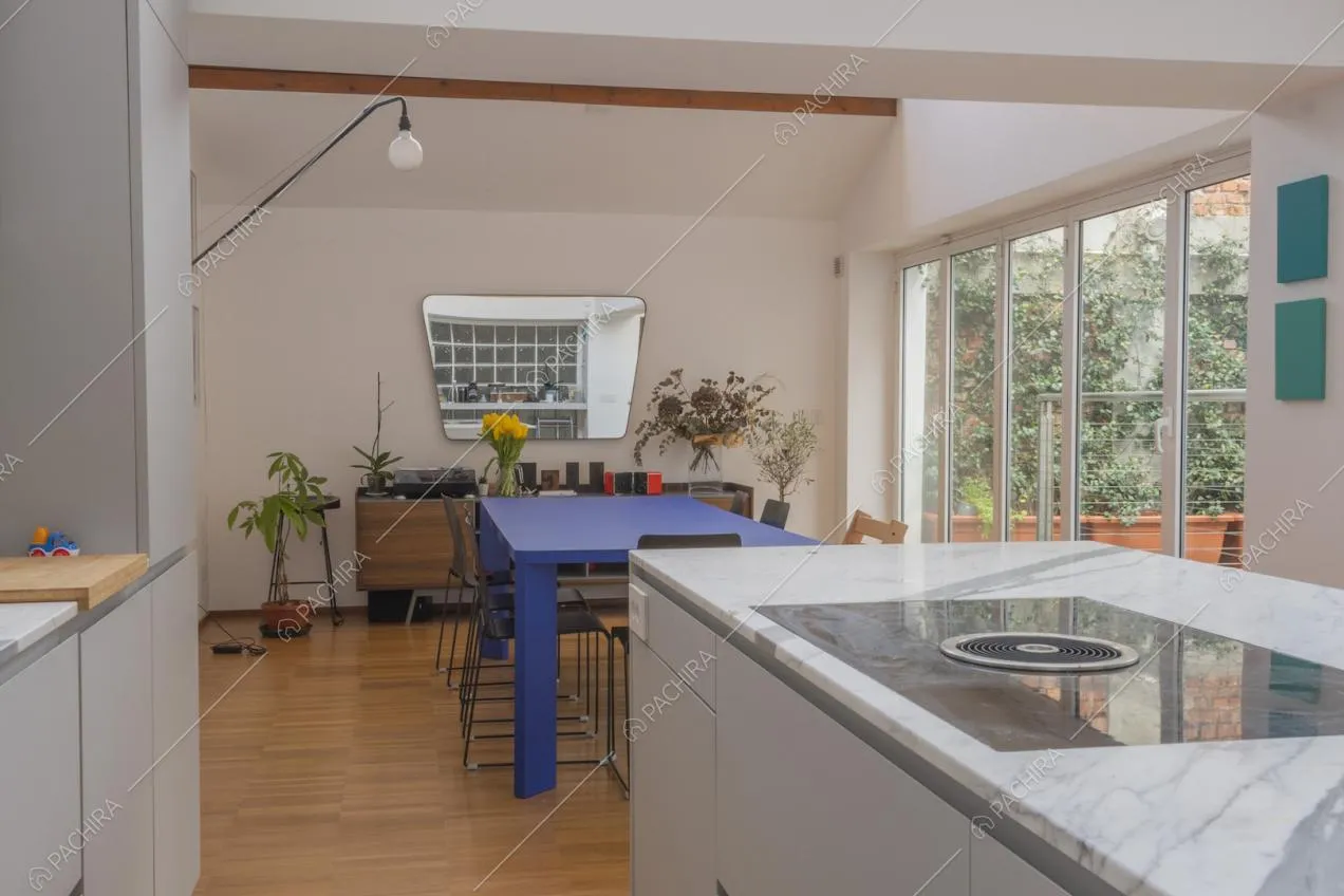 Zona pranzo con parete finestrata e specchio irregolare vista dalla cucina a isola