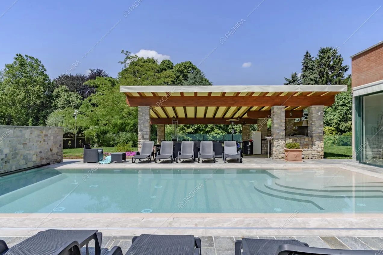 Vista sulla piscina della location, con lettini neri, sul pergolato e sulle ampie vetrate che illuminano gli interni