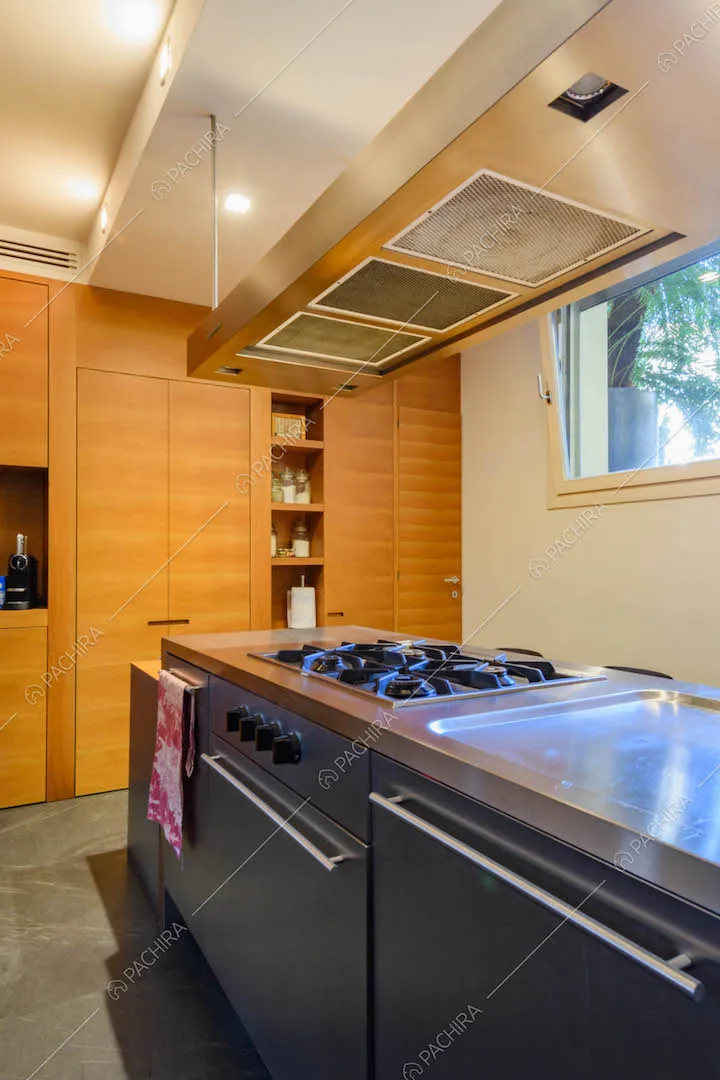 Isola in acciaio con fornelli a gas nella cucina con parete bianca e parete in legno