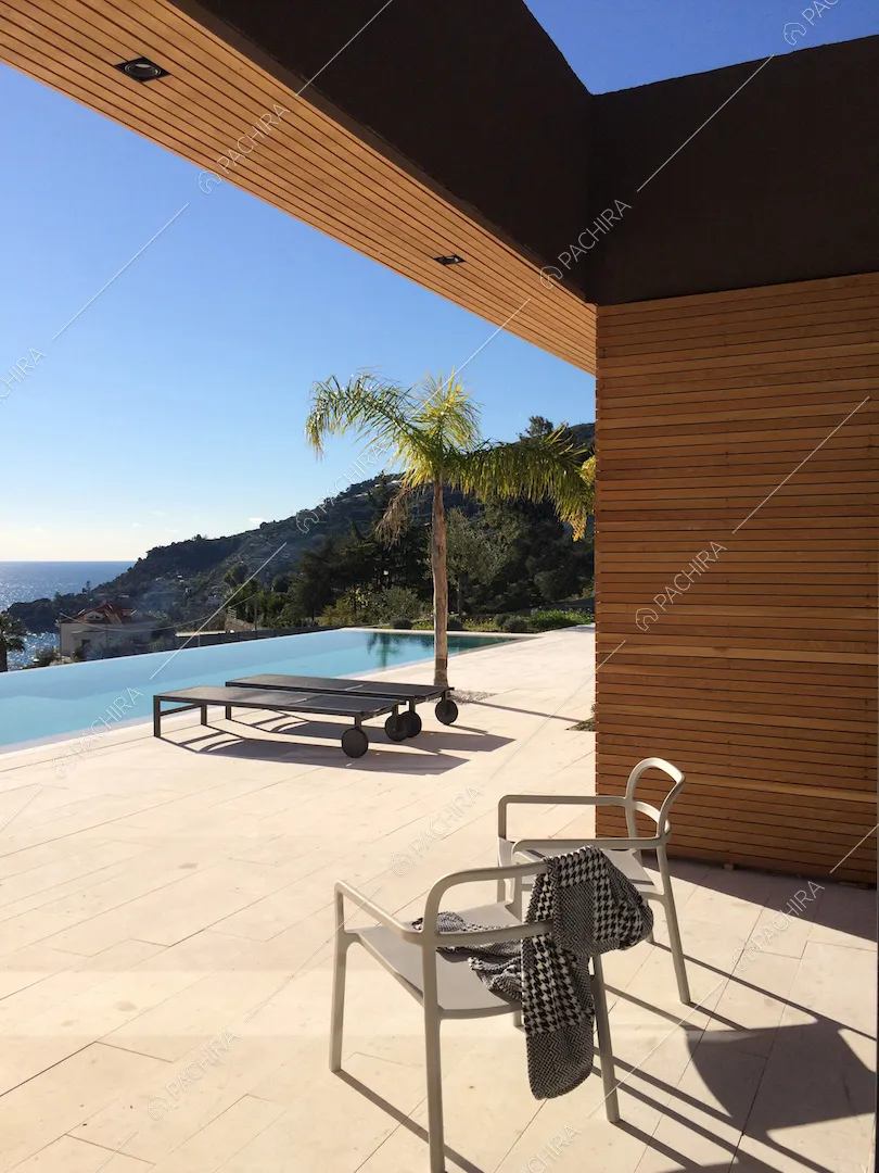 Terrazza con lastre di pietra bianca, sedie, lettini, palme e piscina a sfioro vista mare