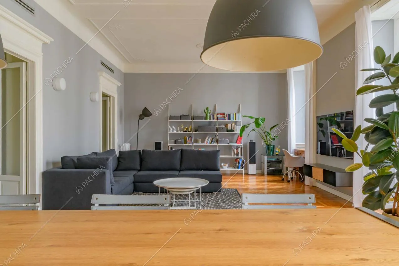 Dal tavolo da pranzo vista sul salotto con divano nero angolare e pavimento in parquet