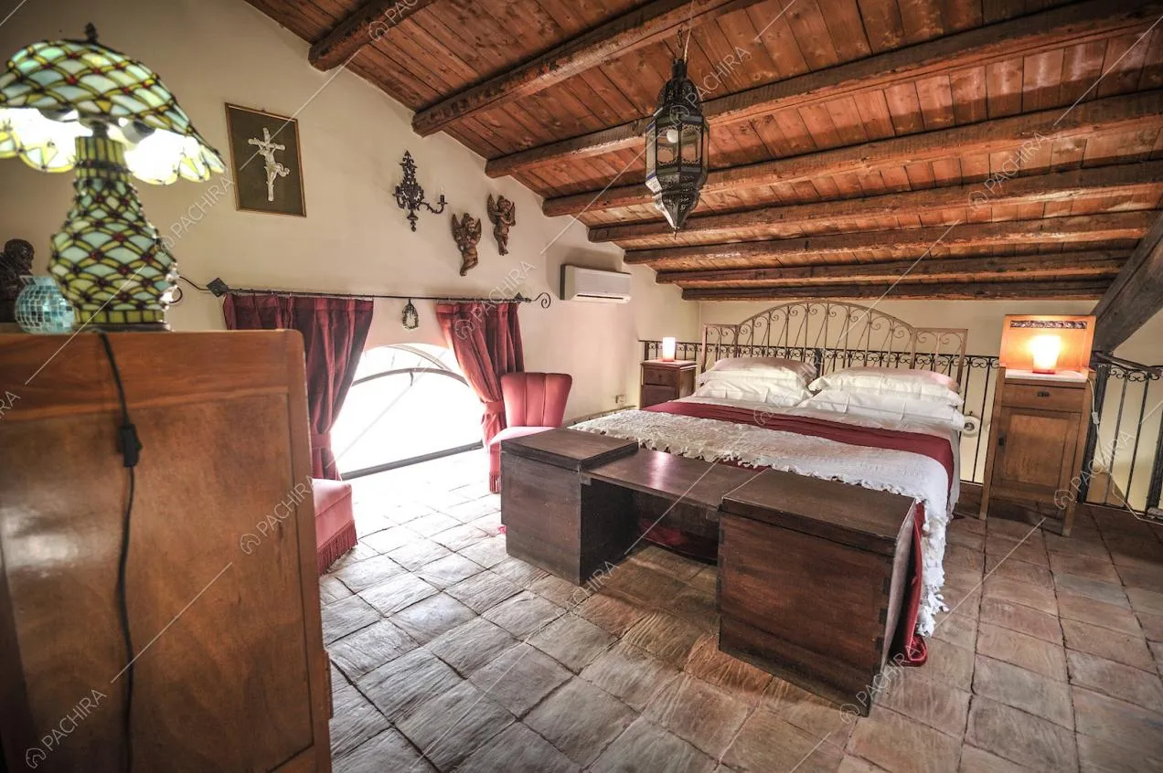 Letto matrimoniale, mobili in legno e poltroncine rosse su pavimento in cotto